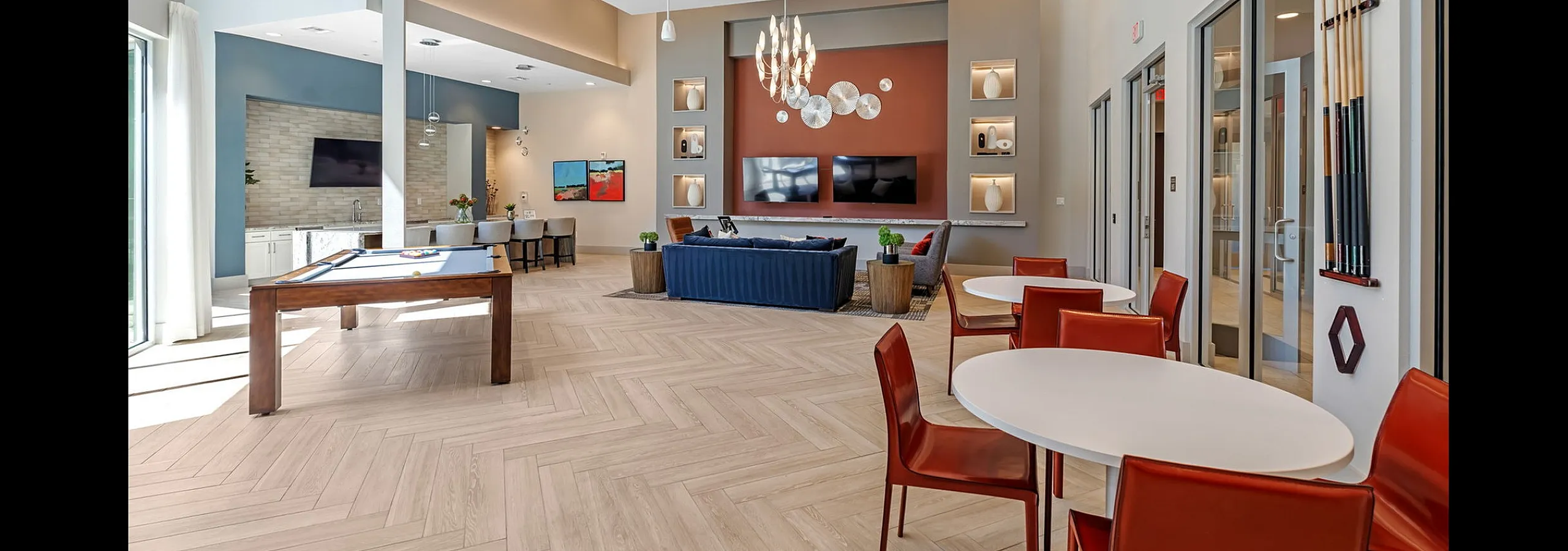 Modern communal lounge with high ceilings, elegant chandeliers, a billiards table, and stylish seating areas enhanced by natural light.