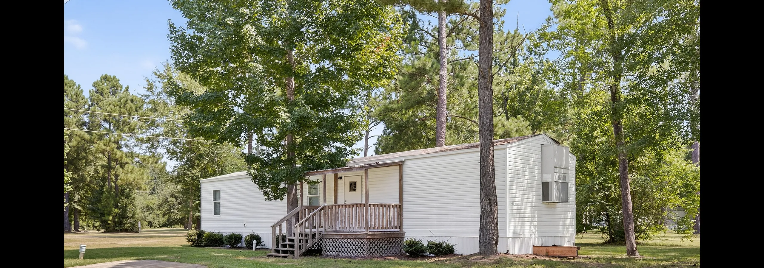 Charming mobile home nestled among tall trees, featuring a cozy porch and lush green surroundings, ideal for serene country living.