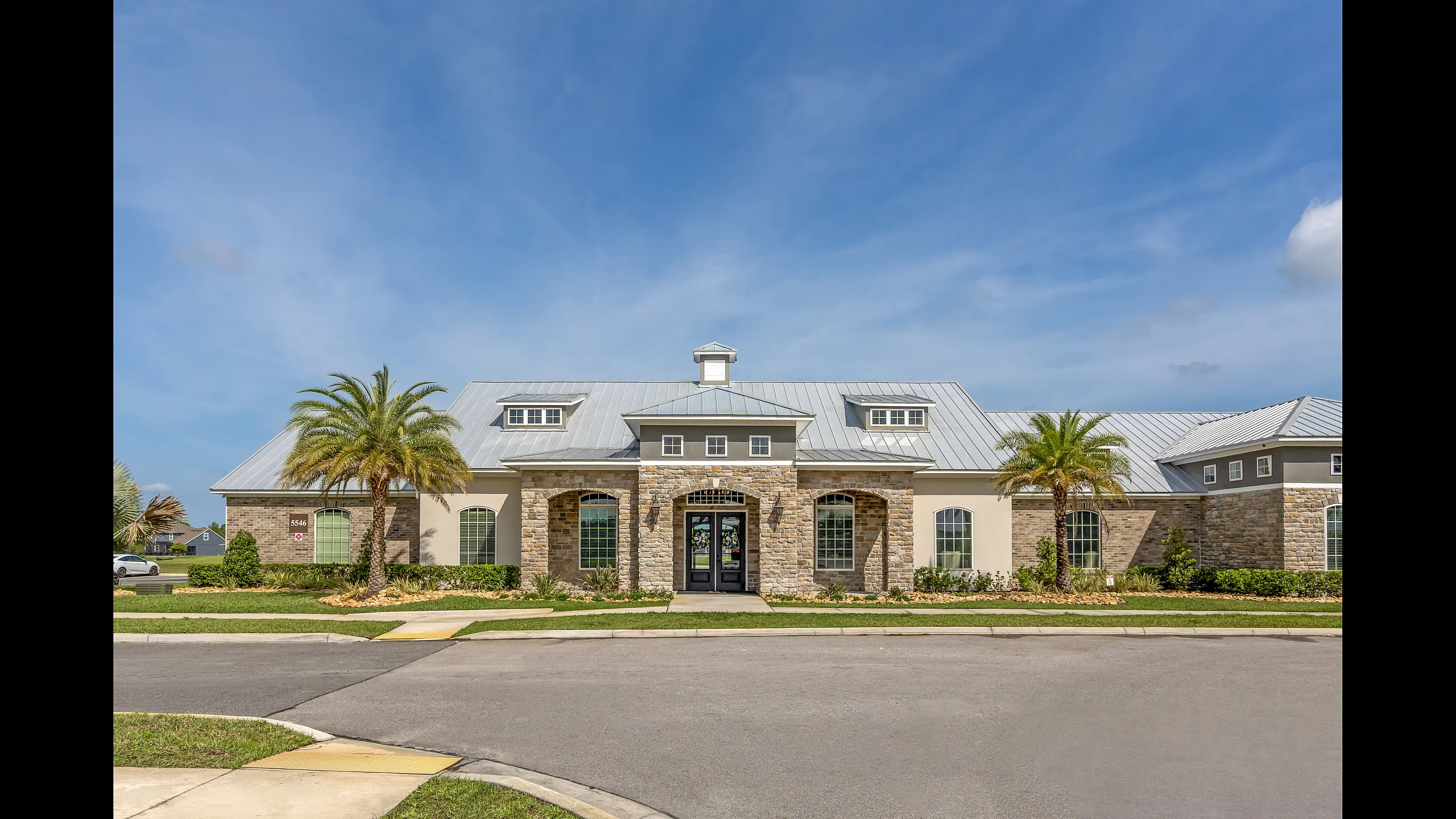Elegant clubhouse exterior with stone facade, lush palm trees, and clear blue sky, perfect for relaxed living and community gatherings.