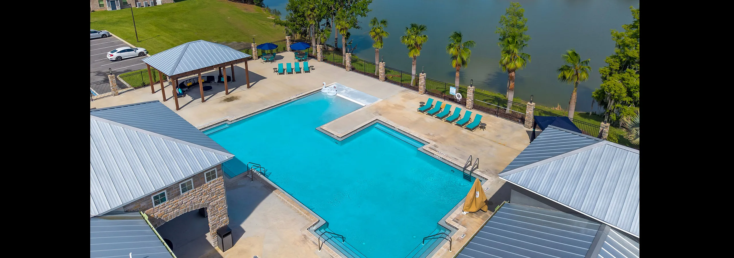 Luxurious apartment complex featuring a sparkling pool, lakeside views, and elegant outdoor seating under shaded pavilions.