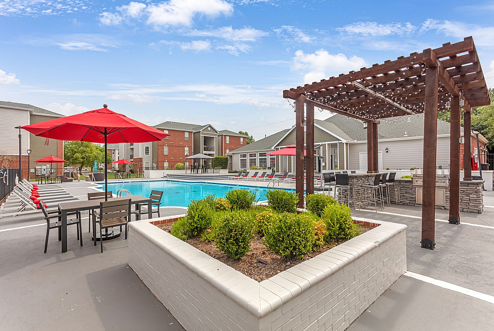 Luxurious outdoor pool area featuring stylish red umbrellas, comfortable lounge chairs, and a charming pergola with seating, perfect for relaxation and entertaining.