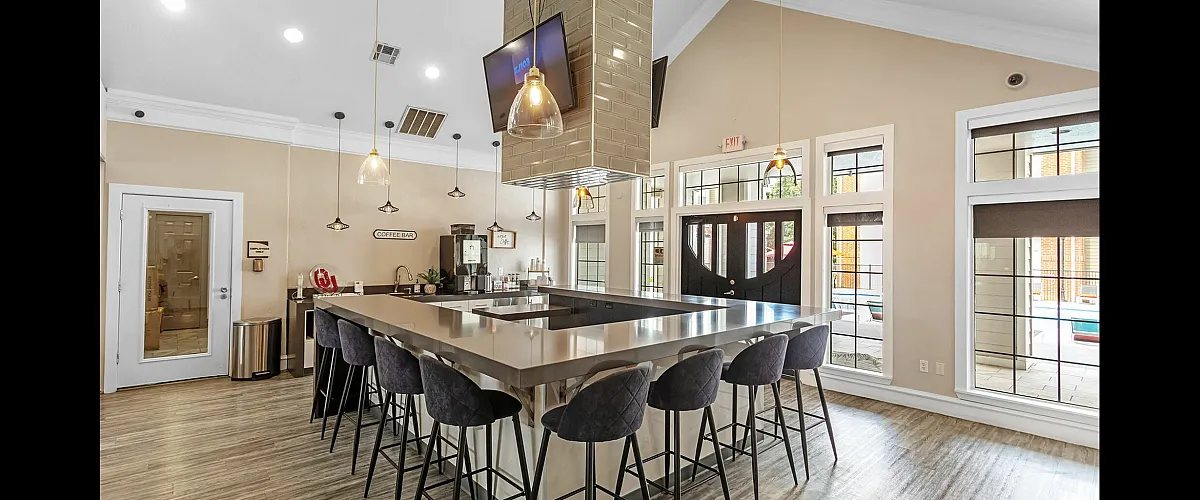 Chic community coffee bar with stylish lighting, high-top seating, and large bright windows overlooking a pool.