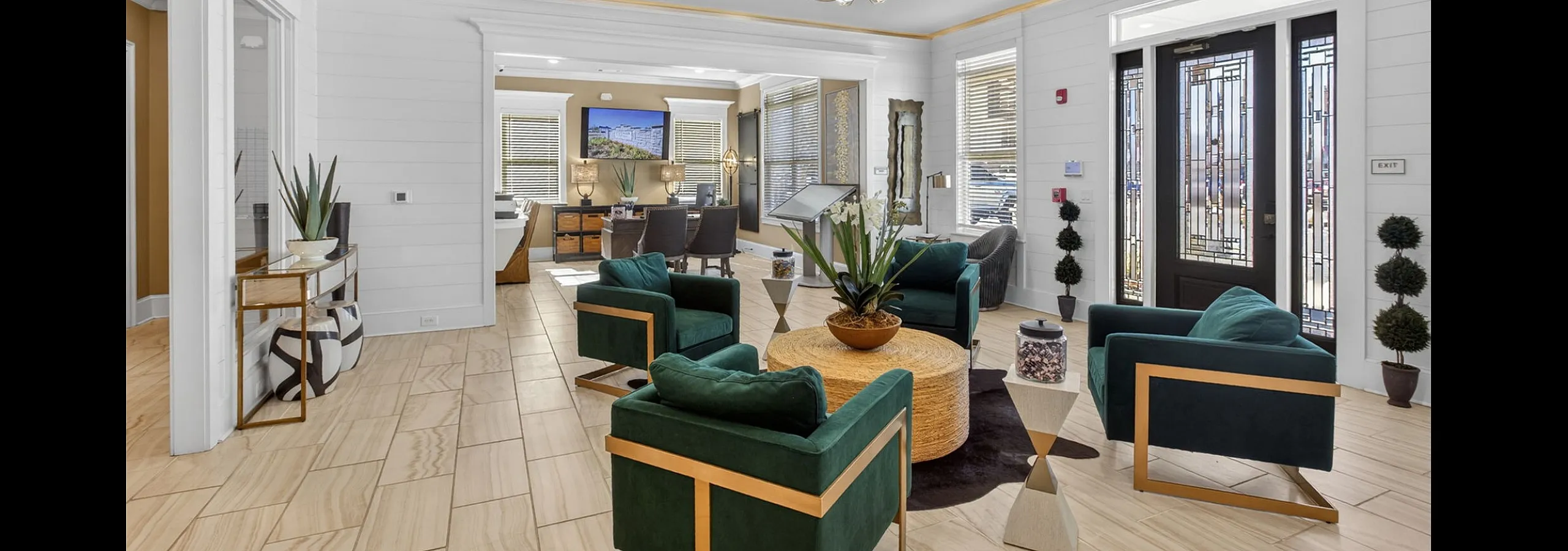 Elegant lobby area featuring velvet green chairs, modern chandelier, and natural light creating a warm and inviting atmosphere.