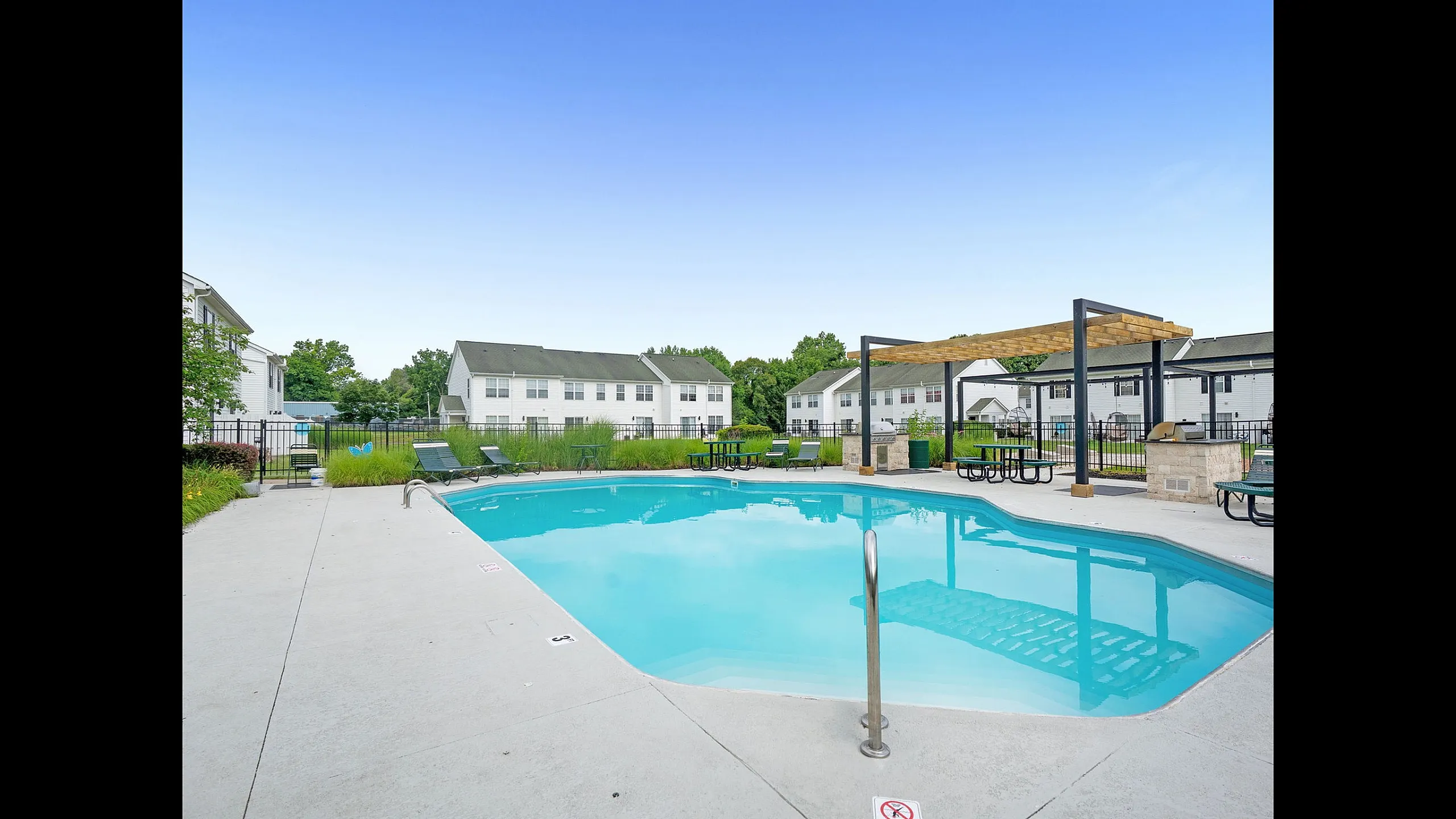 Charming outdoor pool area at a modern apartment complex, featuring comfortable lounge chairs and a stylish pergola in a serene setting.