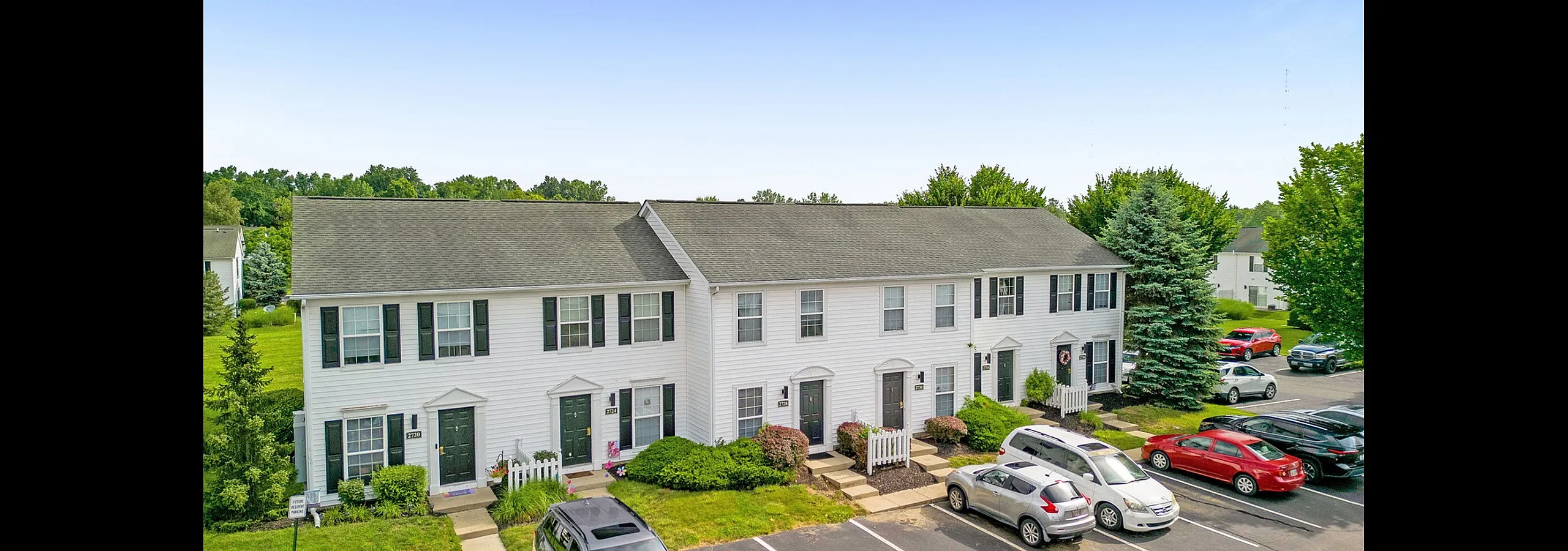 Charming townhouse complex with stylish white facades and lush green surroundings, featuring ample parking and inviting entrances.