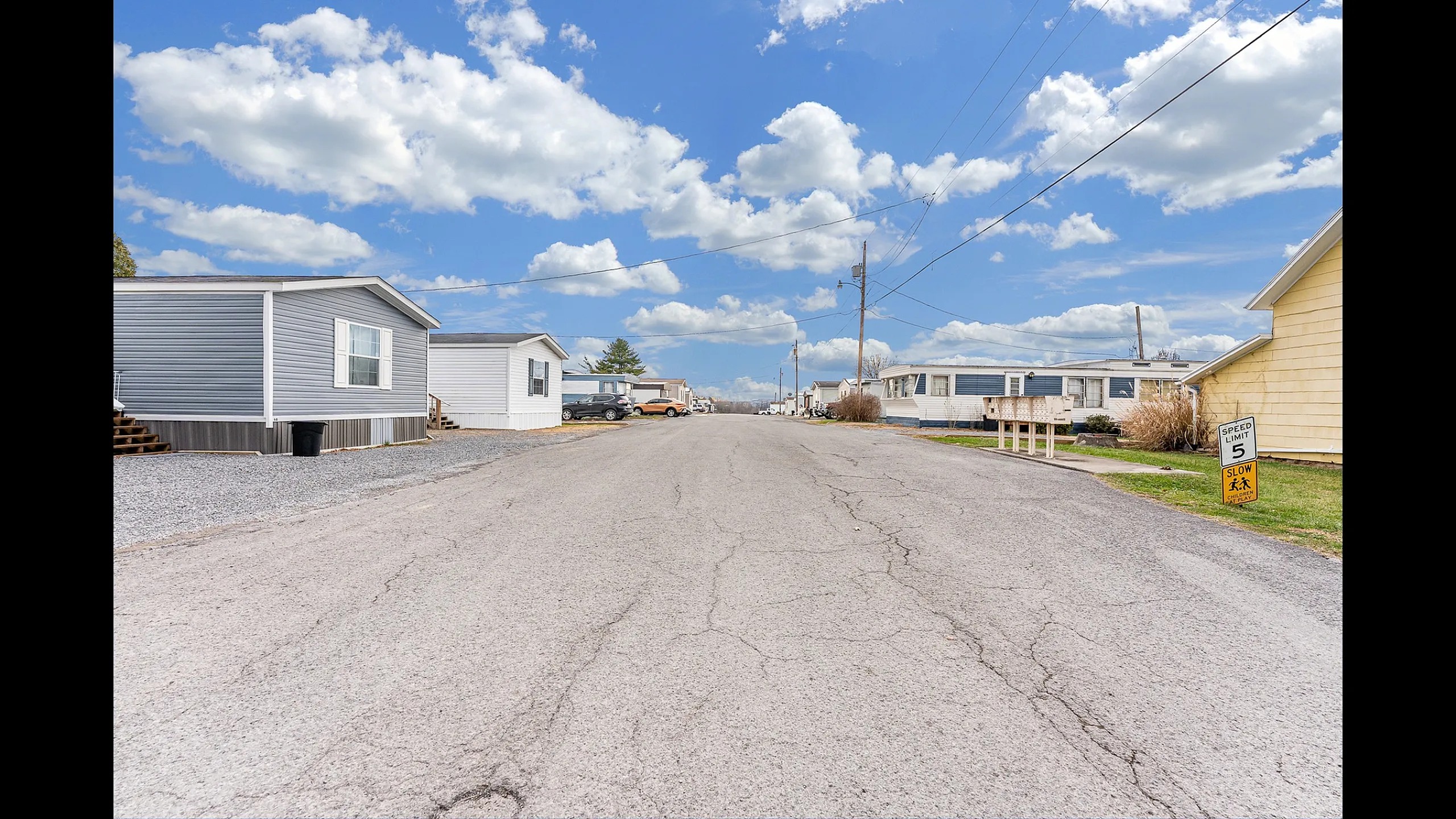 Scenic suburban view of a tranquil mobile home community under a bright blue sky with fluffy clouds, highlighting modern residences and a well-paved road.