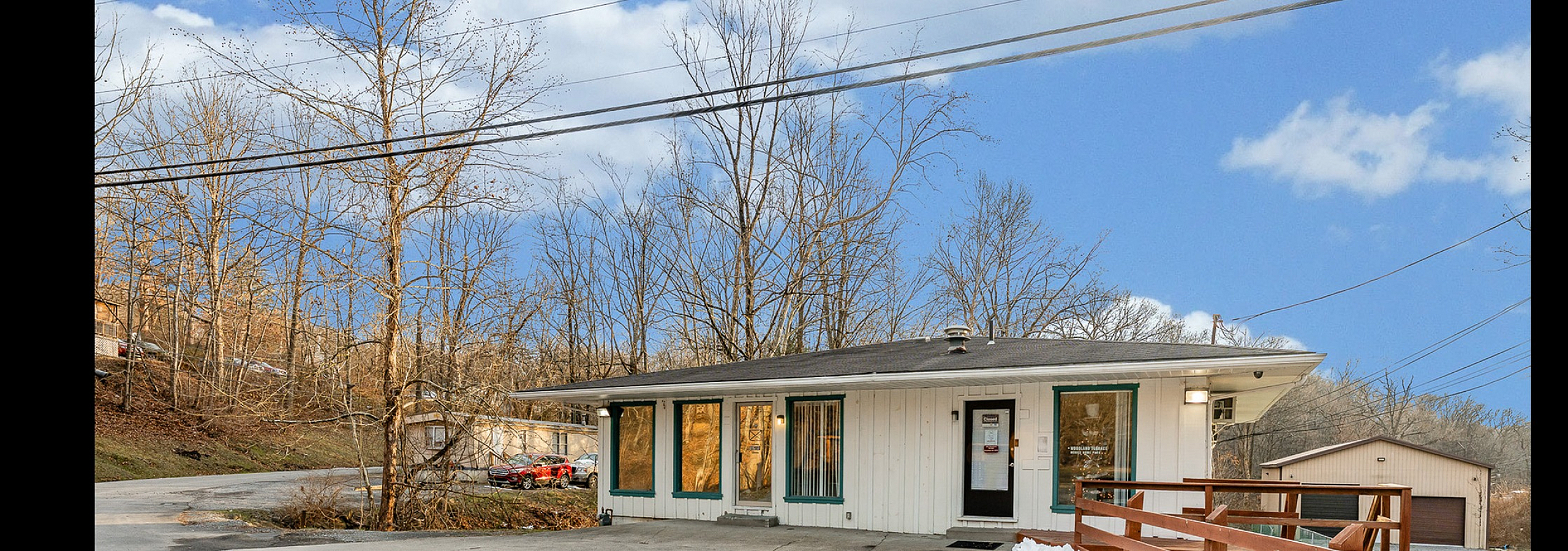 Charming single-story home with large windows and snowy driveway, set against a serene wooded backdrop.