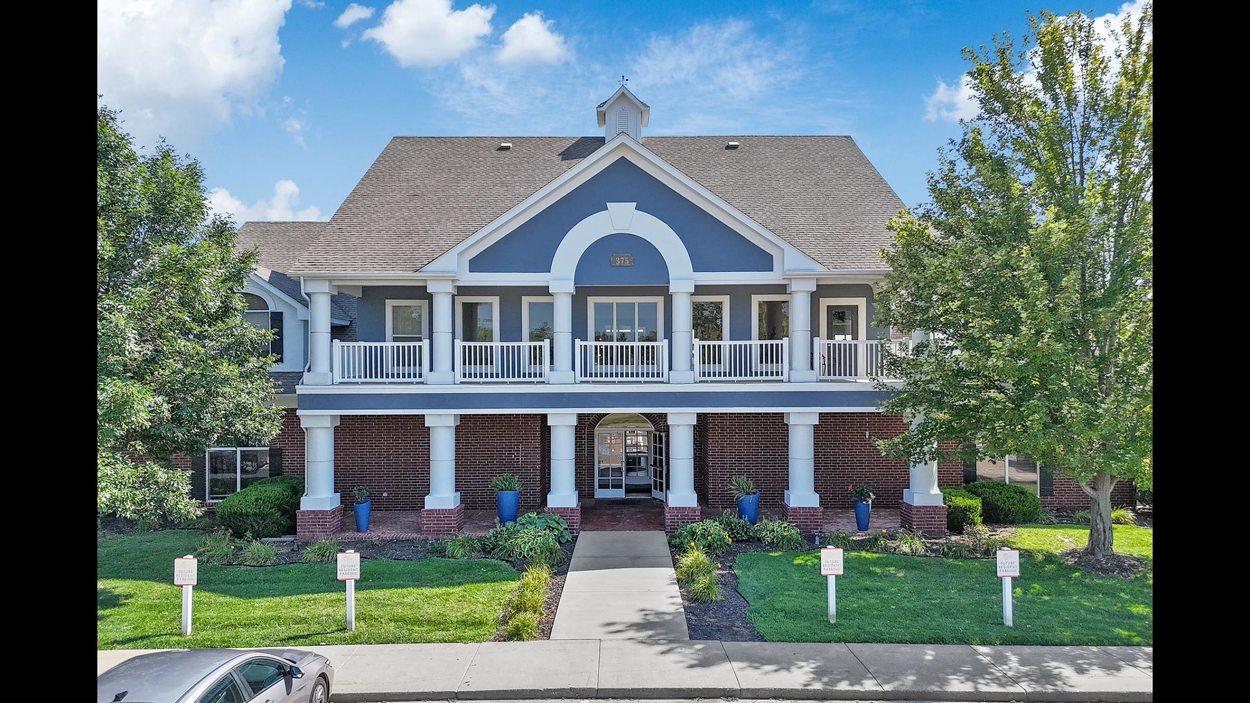 Charming two-story building with elegant columns, manicured landscaping, and a welcoming front entrance, set against a clear blue sky.