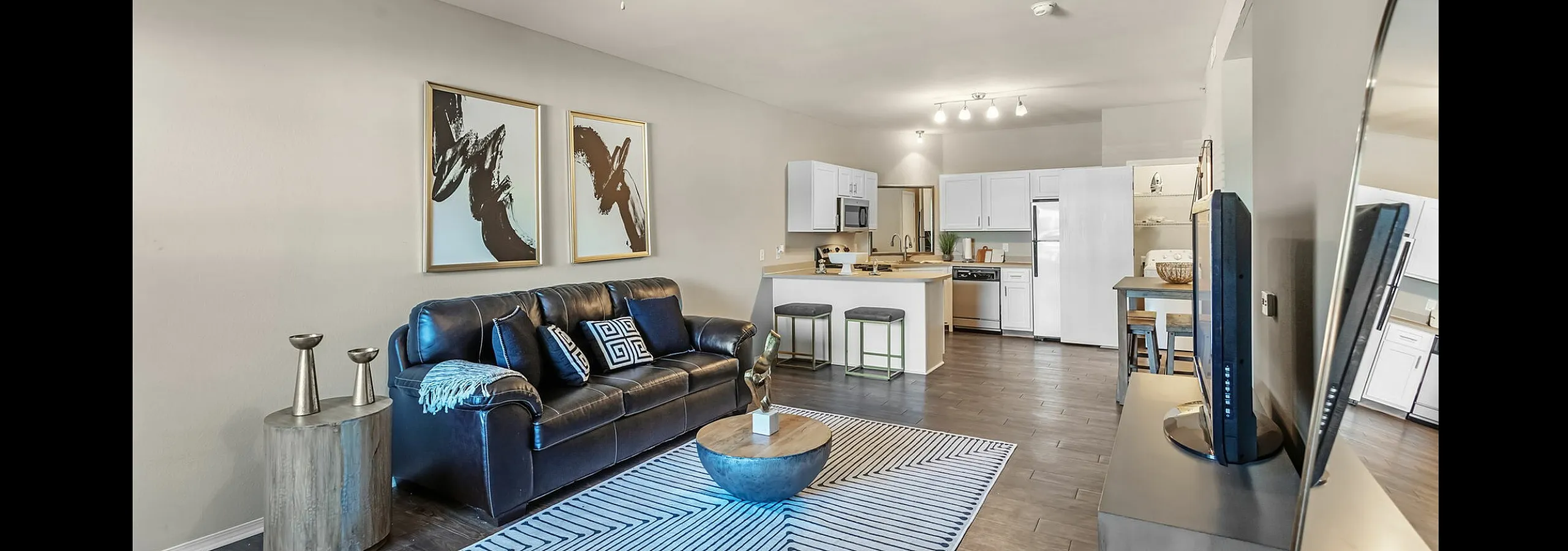 Modern open-concept living room with a sleek leather sofa, stylish decor, and a contemporary kitchen with bar seating.