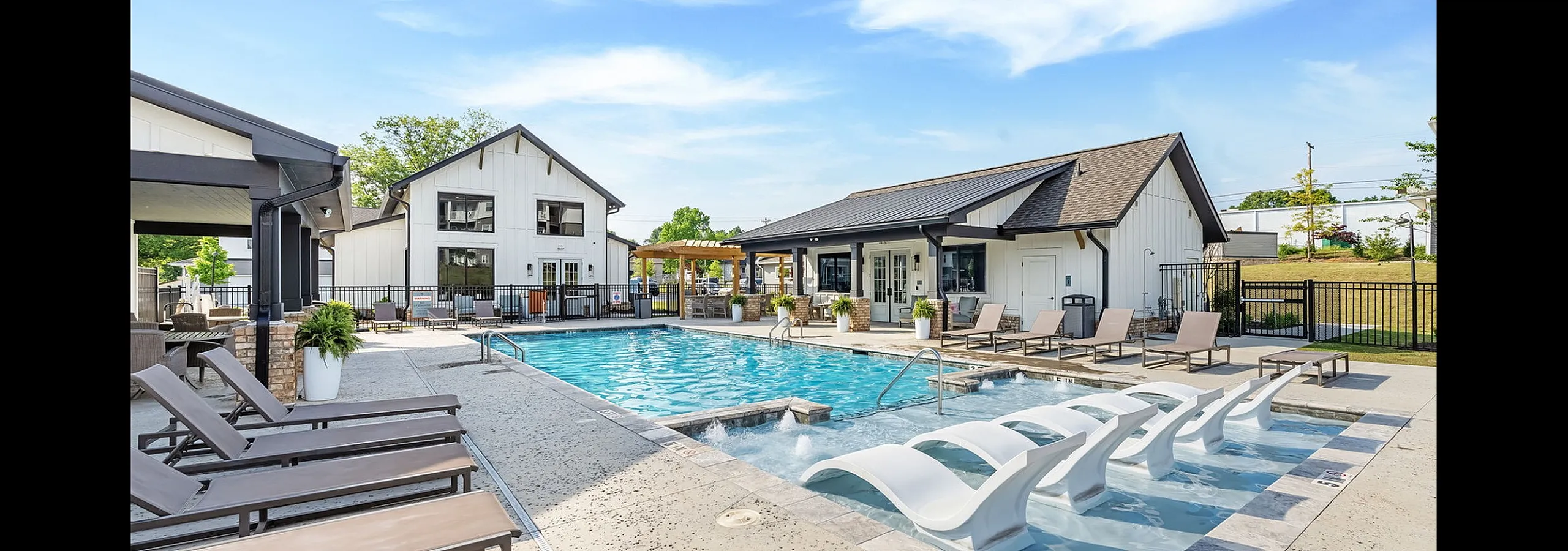 Luxurious outdoor pool area featuring stylish lounge chairs, modern clubhouse, and bright blue skies, perfect for relaxation and social gatherings.