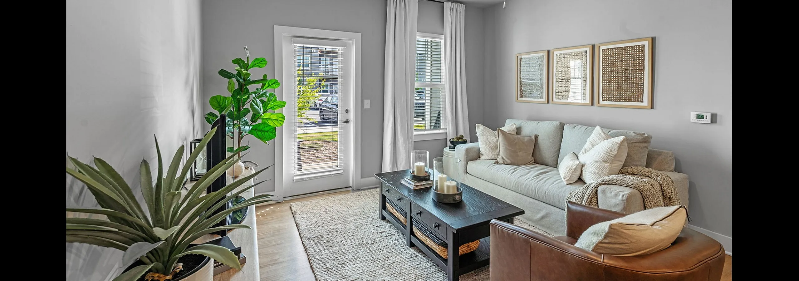 Bright, contemporary living room with a cozy beige sofa, elegant decor, large floor plant, and natural light streaming through a glass door.