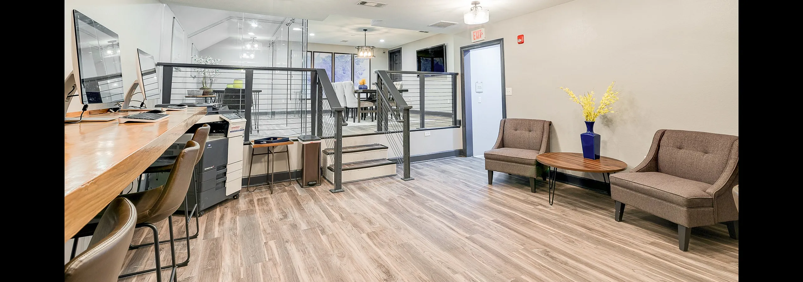 Modern office space with sleek wooden flooring, stylish seating area, and a bright, open layout featuring a glass-walled meeting area.