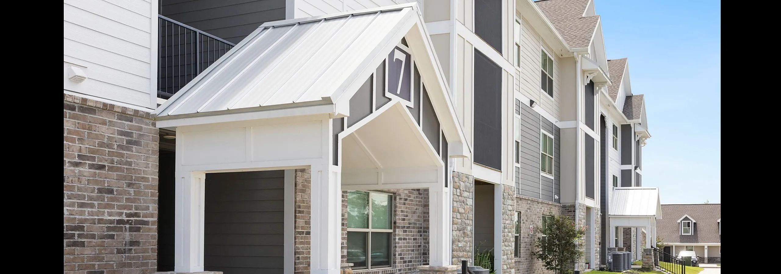 Modern apartment exterior featuring stylish architecture with white and gray siding and stone accents under a clear blue sky.