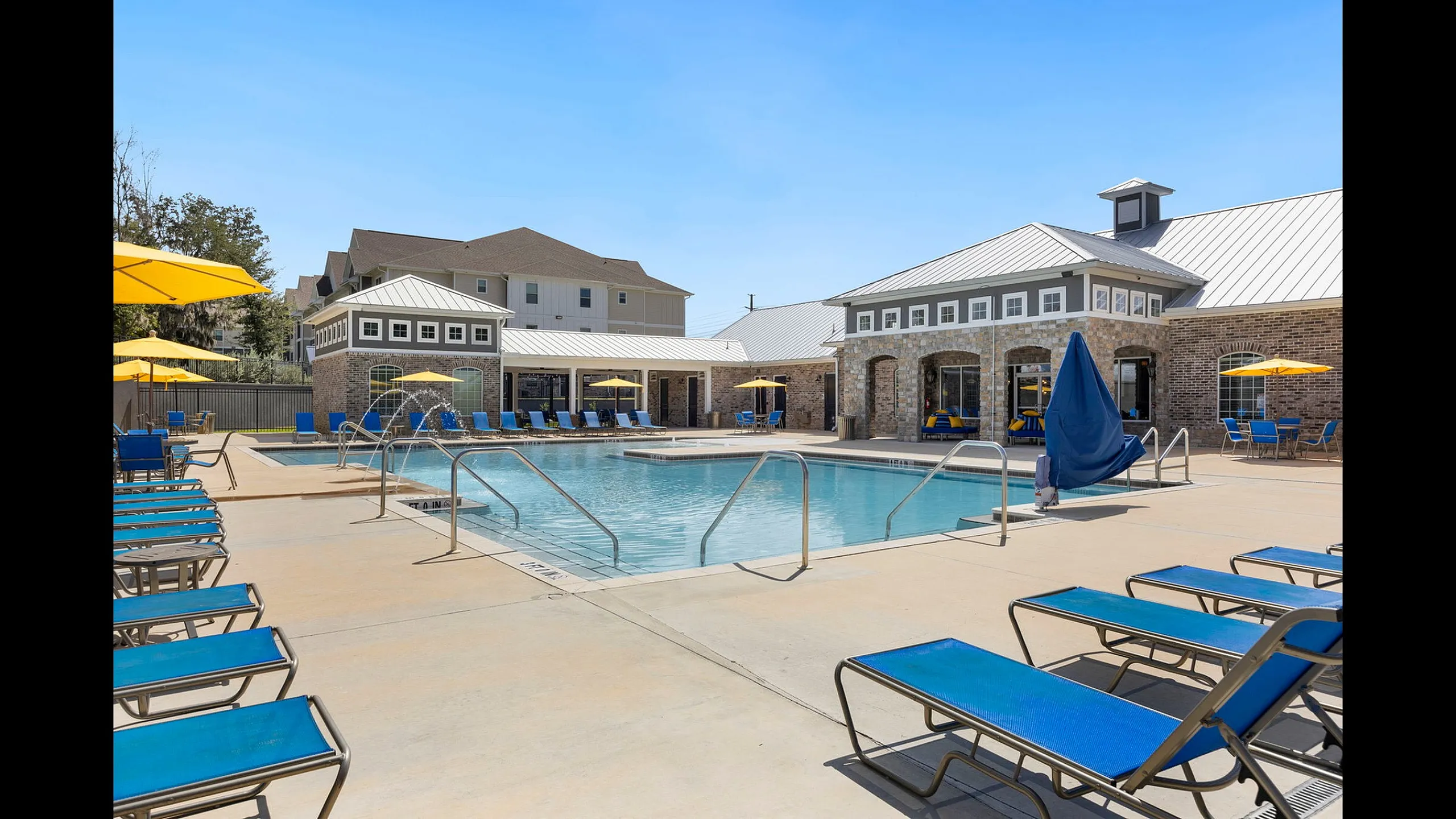 Chic apartment complex featuring a sparkling outdoor pool with vibrant blue lounge chairs and yellow umbrellas, perfect for relaxation and leisure.