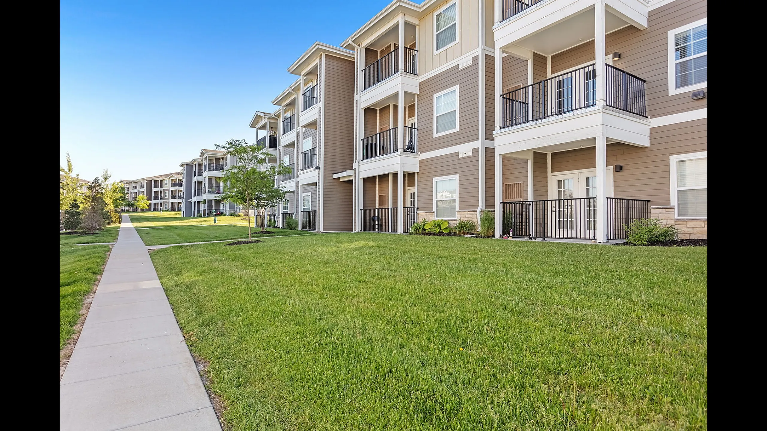 Charming, modern apartment exterior with inviting balconies overlooking lush green lawns and a scenic pathway.