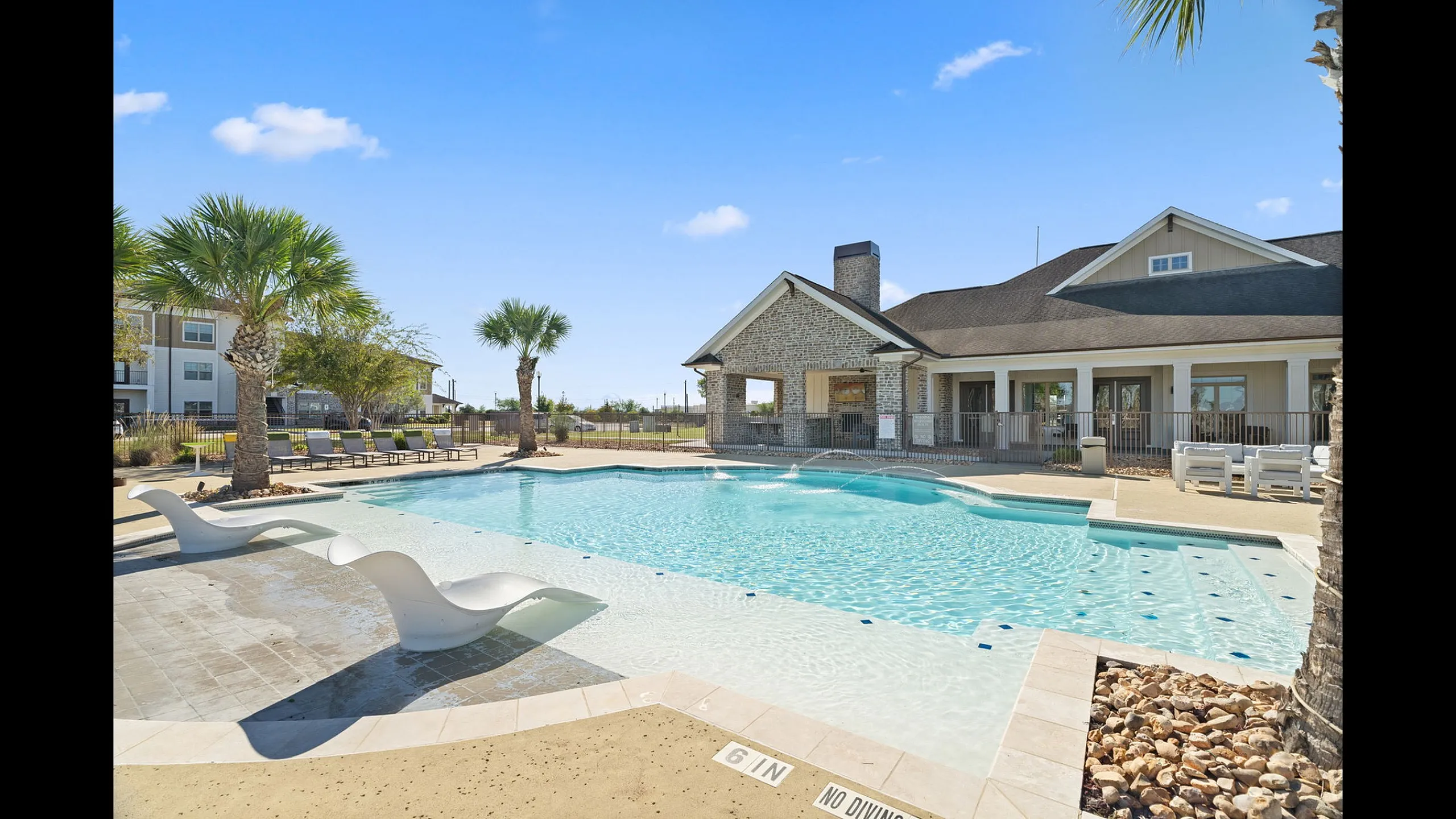 Luxurious apartment community pool area with elegant lounge chairs, surrounded by palm trees and modern clubhouse.