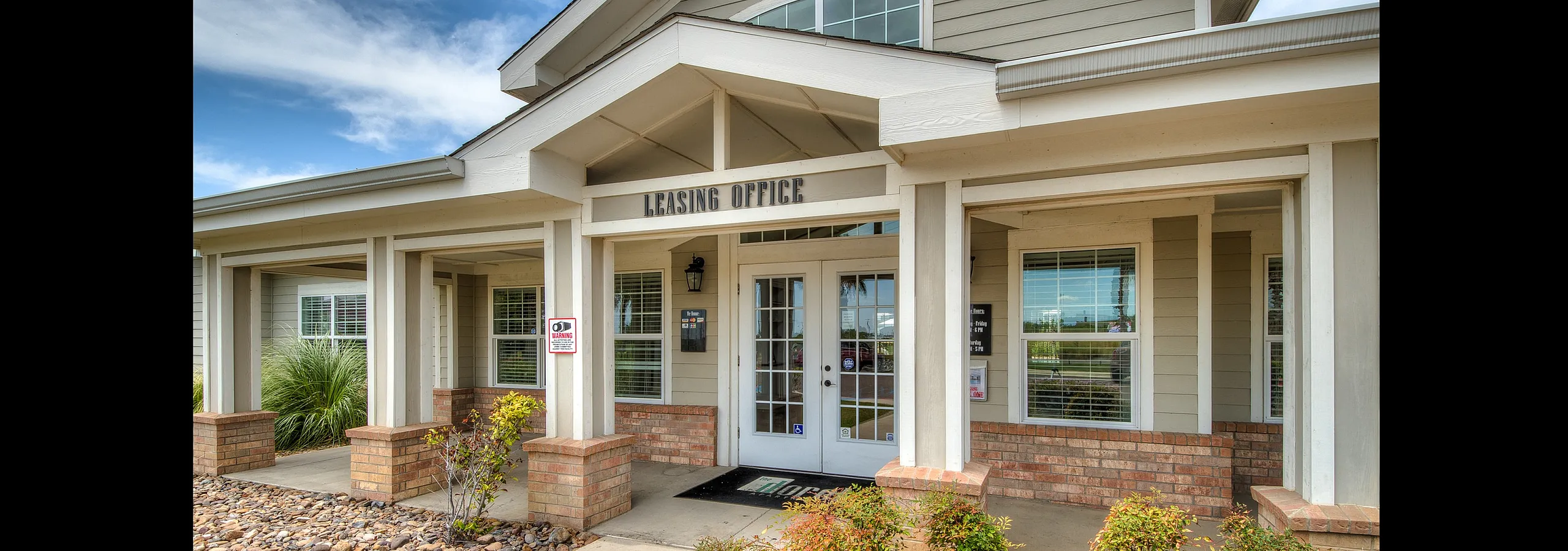Inviting leasing office entrance with charming architectural details, surrounded by lush landscaping and vibrant flowers.