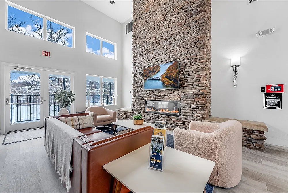 Elegant living room with a tall stone fireplace, modern furnishings, and large windows offering a scenic view.