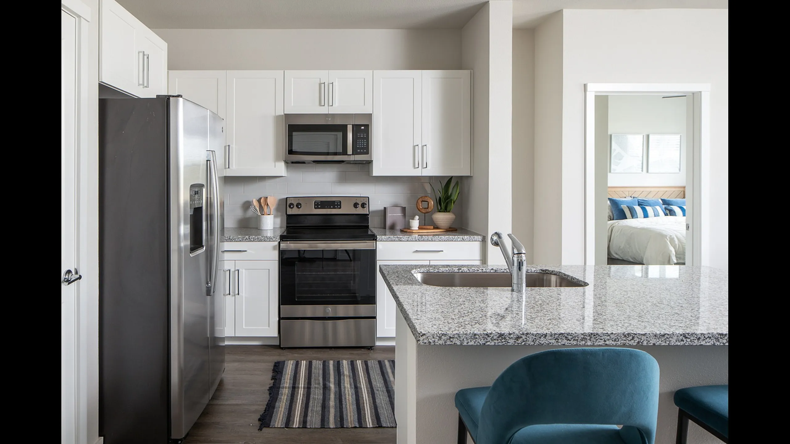 Modern kitchen with sleek stainless steel appliances, granite countertops, and stylish white cabinets, leading to a cozy bedroom.