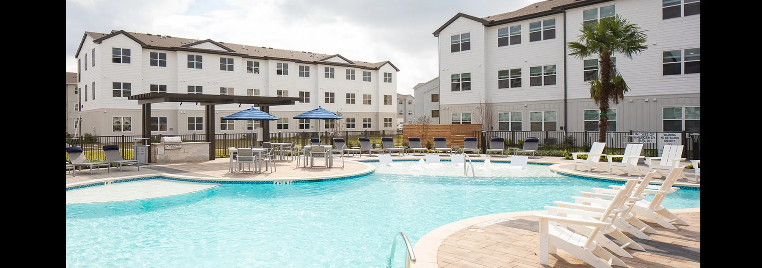Inviting apartment complex featuring a sparkling outdoor pool with lounge chairs, surrounded by modern multi-story buildings and lush greenery.