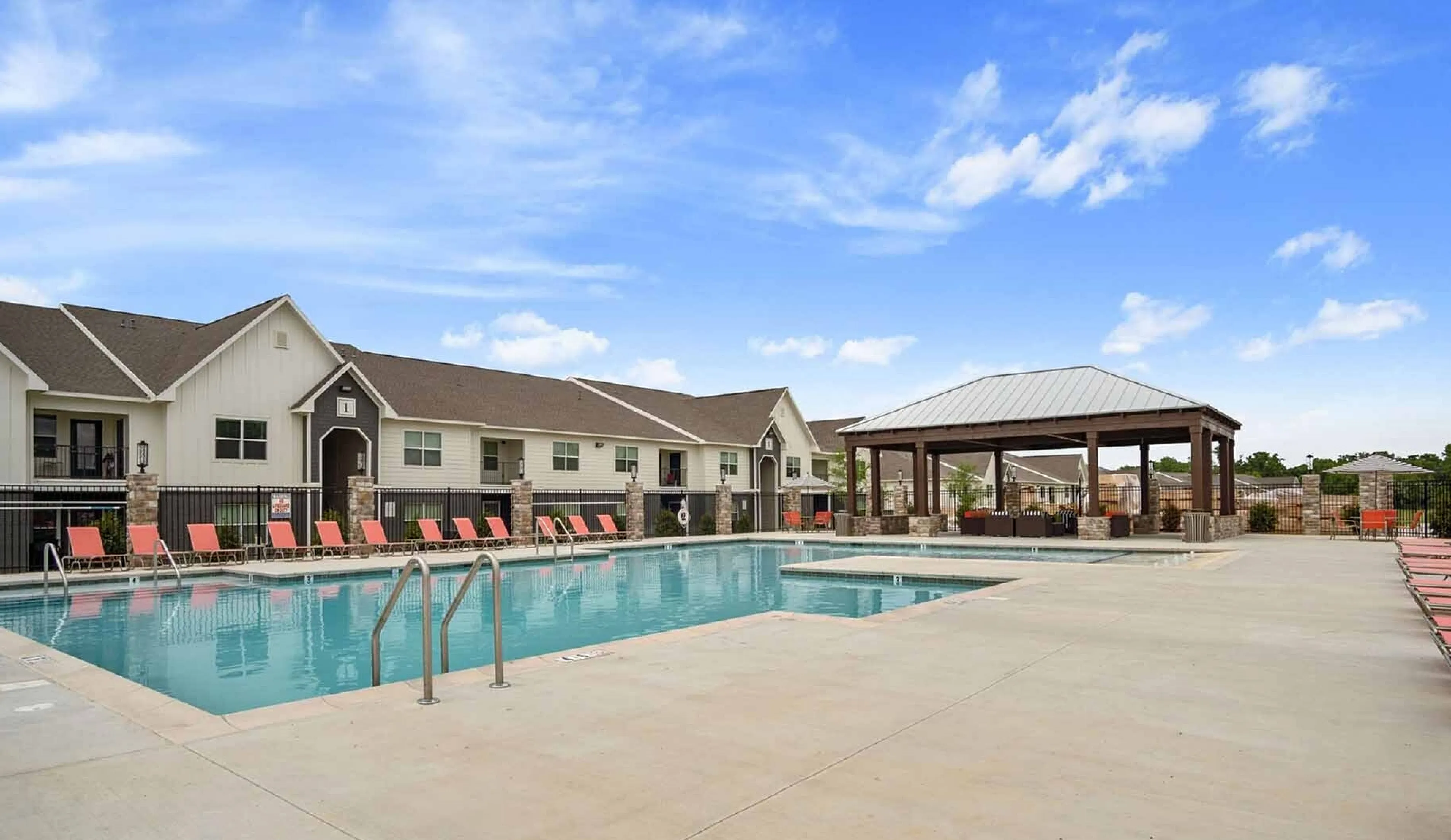 Inviting apartment complex featuring a sparkling swimming pool with modern lounge chairs under a vibrant blue sky.