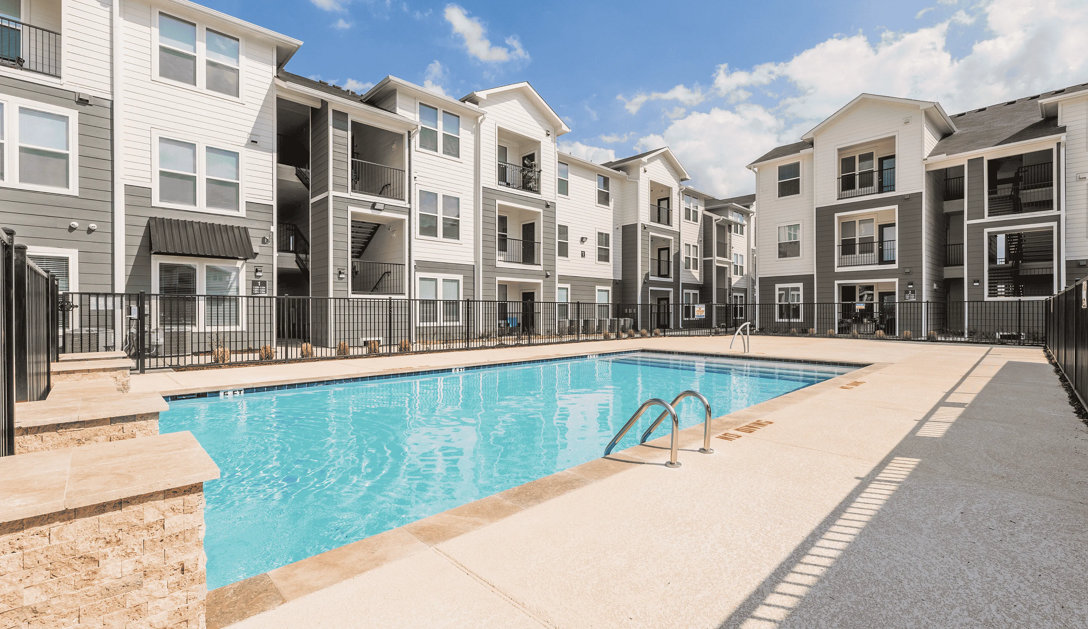Modern apartment complex with elegant architecture featuring a sparkling swimming pool under a clear blue sky.