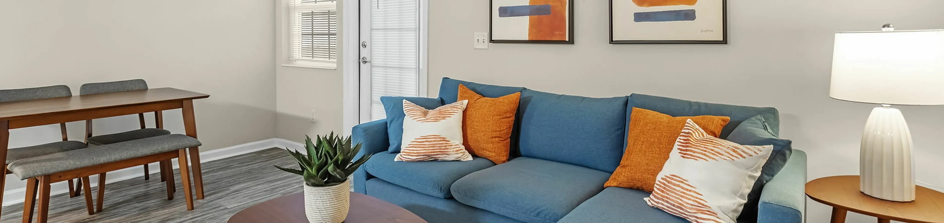 Modern living room with vibrant blue sofa, stylish artwork, and a cozy dining area, perfect for relaxation and entertaining.