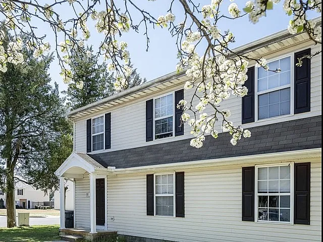 Charming suburban home with white exterior, surrounded by blooming trees and lush greenery.