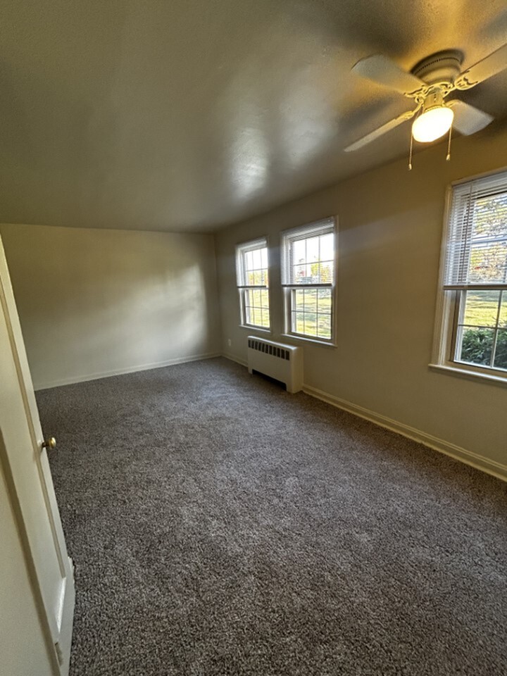 Bright and inviting room with plush carpet, large windows, and a ceiling fan, perfect for cozy living.