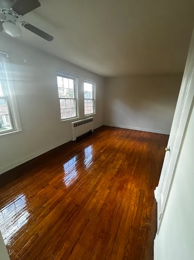 Spacious, sunlit room with polished hardwood floors and large windows, perfect for a cozy atmosphere.