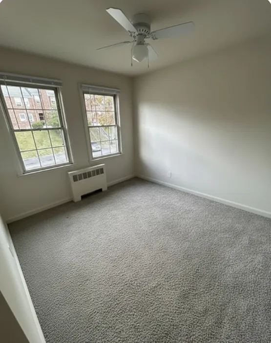 Bright room with large windows, plush carpet, and ceiling fan, perfect for a cozy living space.