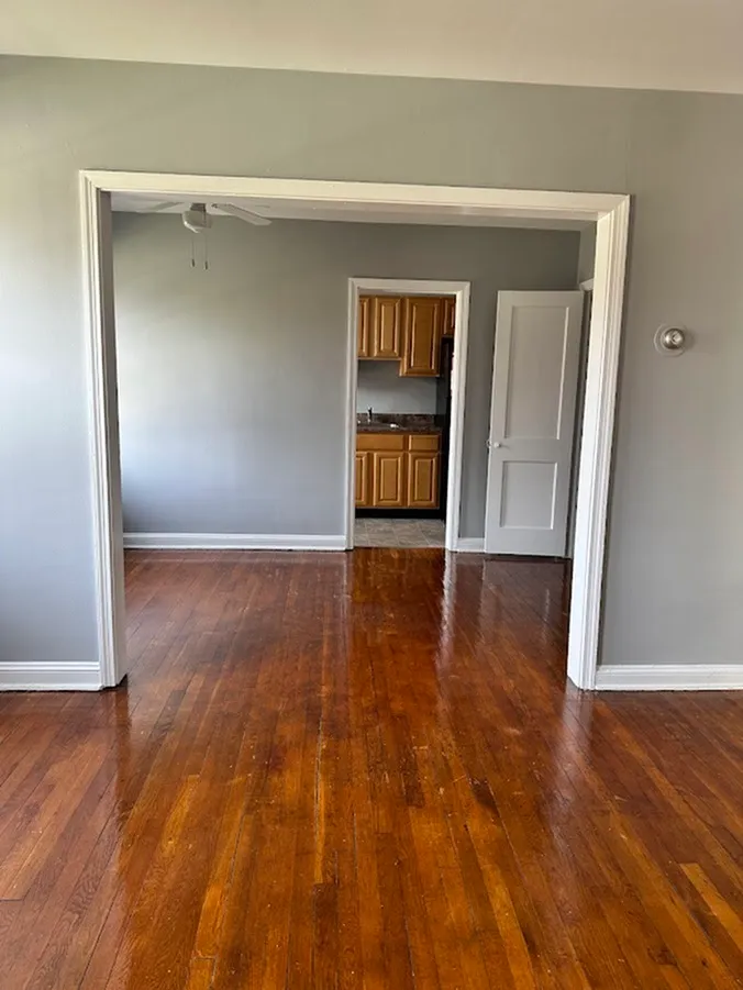 Inviting open-concept living area with gleaming hardwood floors leading to a cozy kitchen with wooden cabinets.