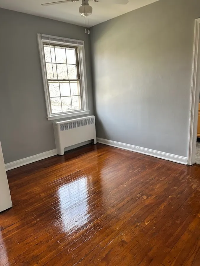 Bright room with polished hardwood floors, a large window, and a ceiling fan, perfect for a cozy and inviting atmosphere.