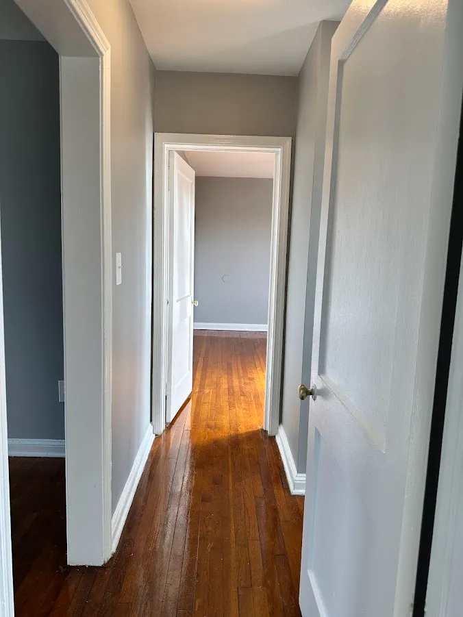 Bright hallway with gleaming wooden floors leading to a sunlit room, perfect for a warm and inviting apartment atmosphere.