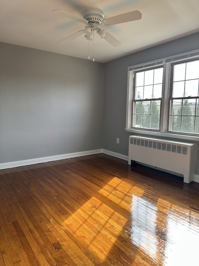 Bright and airy room with polished hardwood floors, modern ceiling fan, and large sunlit windows.