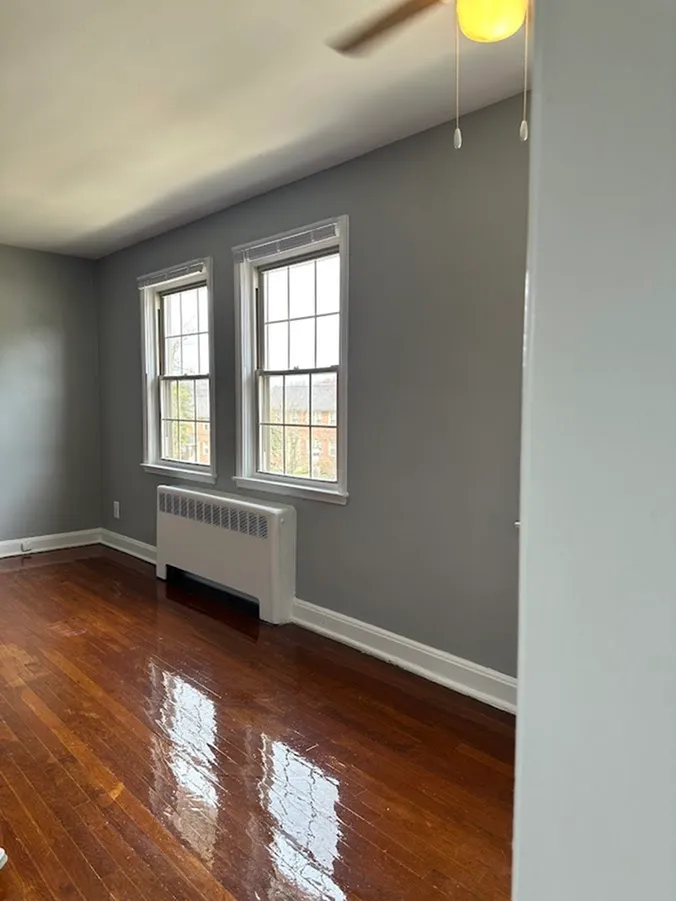 Bright room featuring polished hardwood floors, two large windows, and modern gray walls.