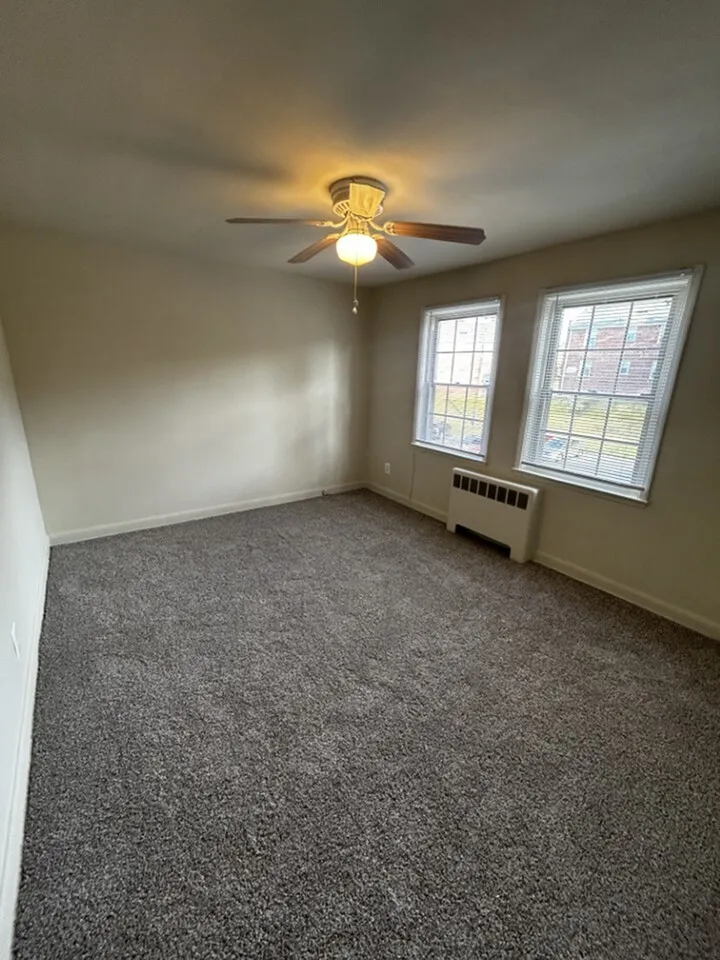 Bright, inviting bedroom with plush carpet, ceiling fan, and large windows letting in natural light.