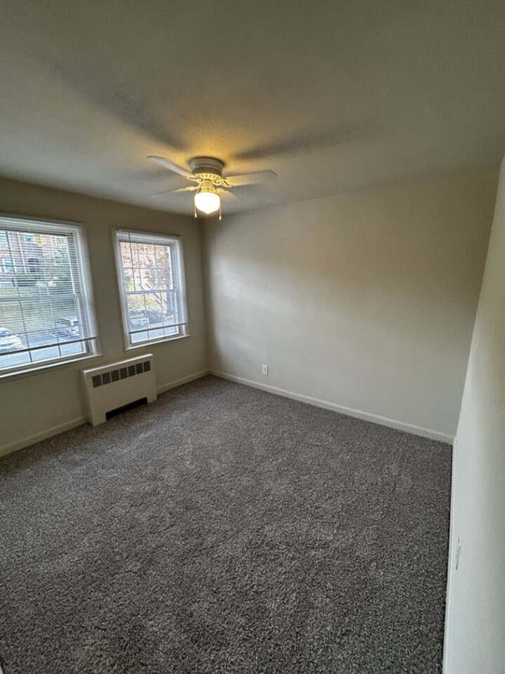 Bright and cozy room with neutral carpet, large windows, and a ceiling fan, offering a welcoming atmosphere and plenty of natural light.
