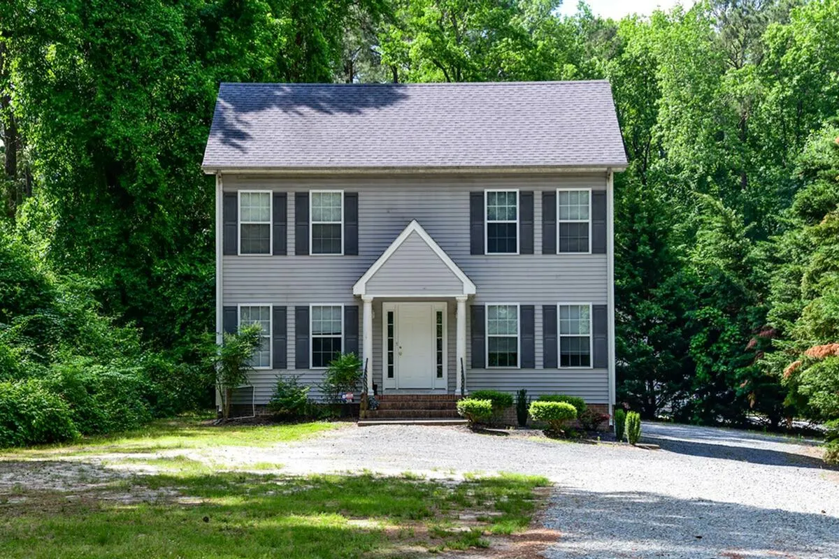 Charming two-story house with a classic gable roof, surrounded by lush greenery and a spacious front yard.