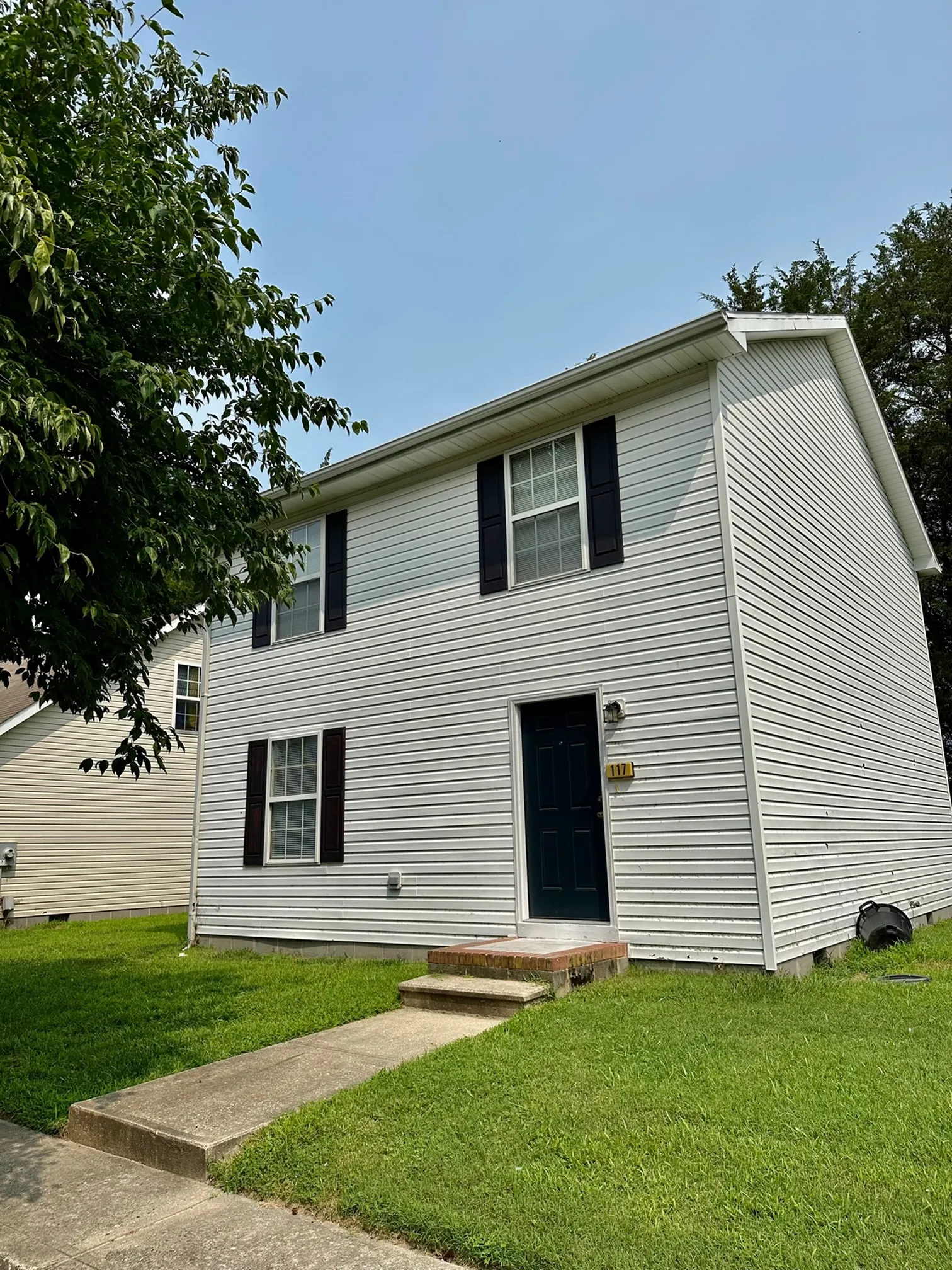 Charming two-story white house with black shutters and a lush green lawn, perfect for families seeking comfort and style.