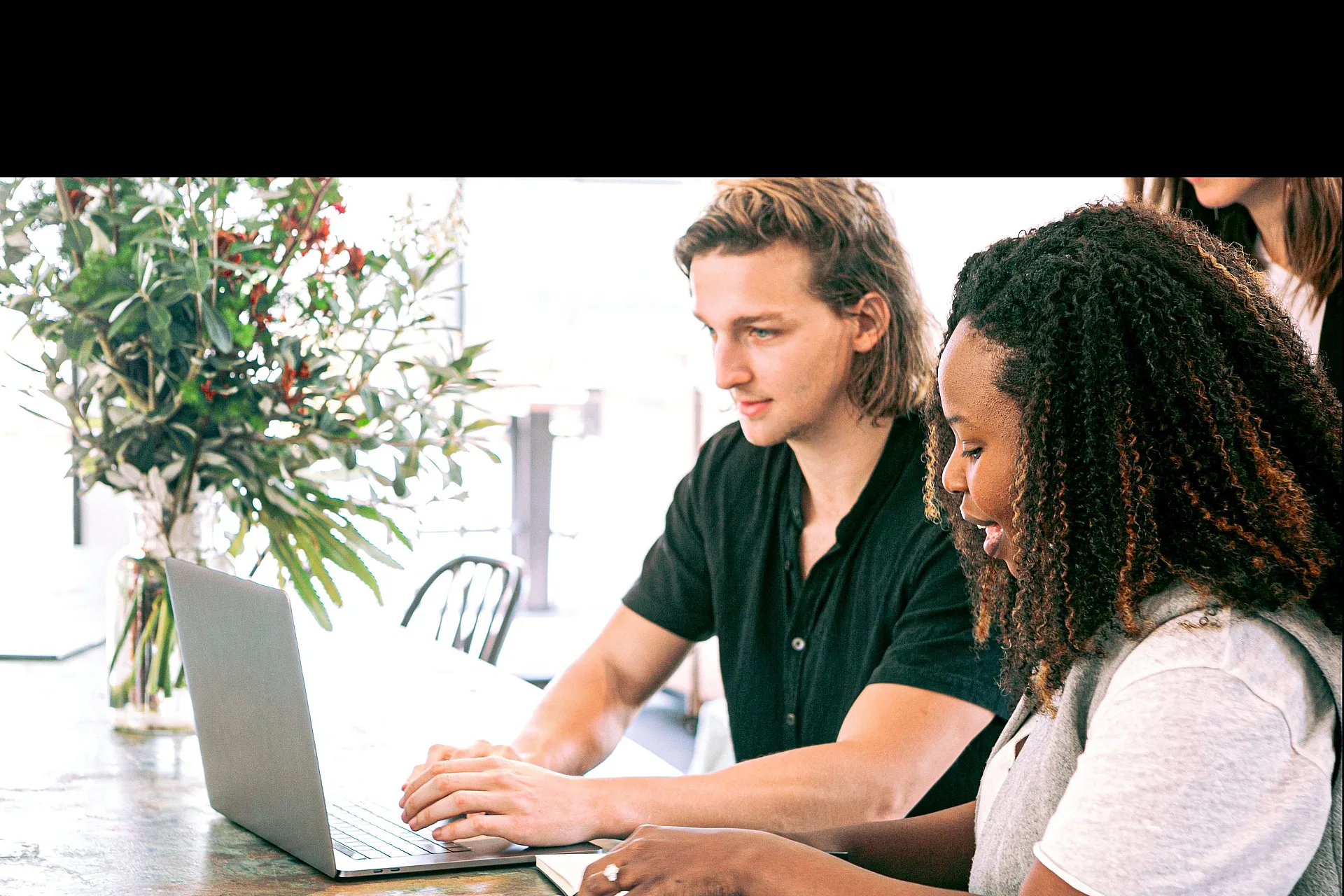 Two people collaborating at a stylish workspace with a laptop and vibrant floral arrangement.