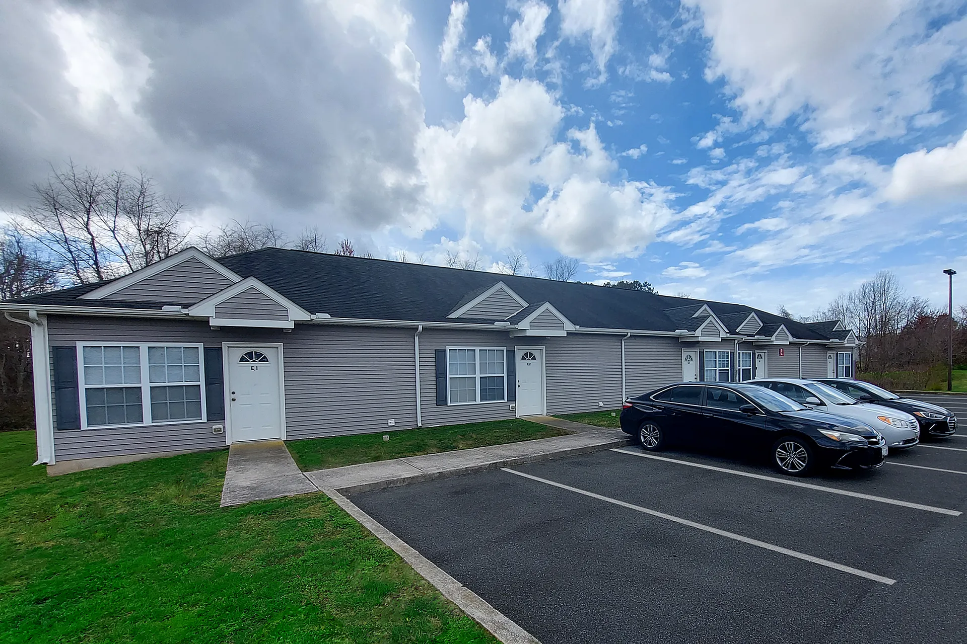 Charming suburban apartment building with a modern exterior, ample parking space, and a scenic view of the sky.