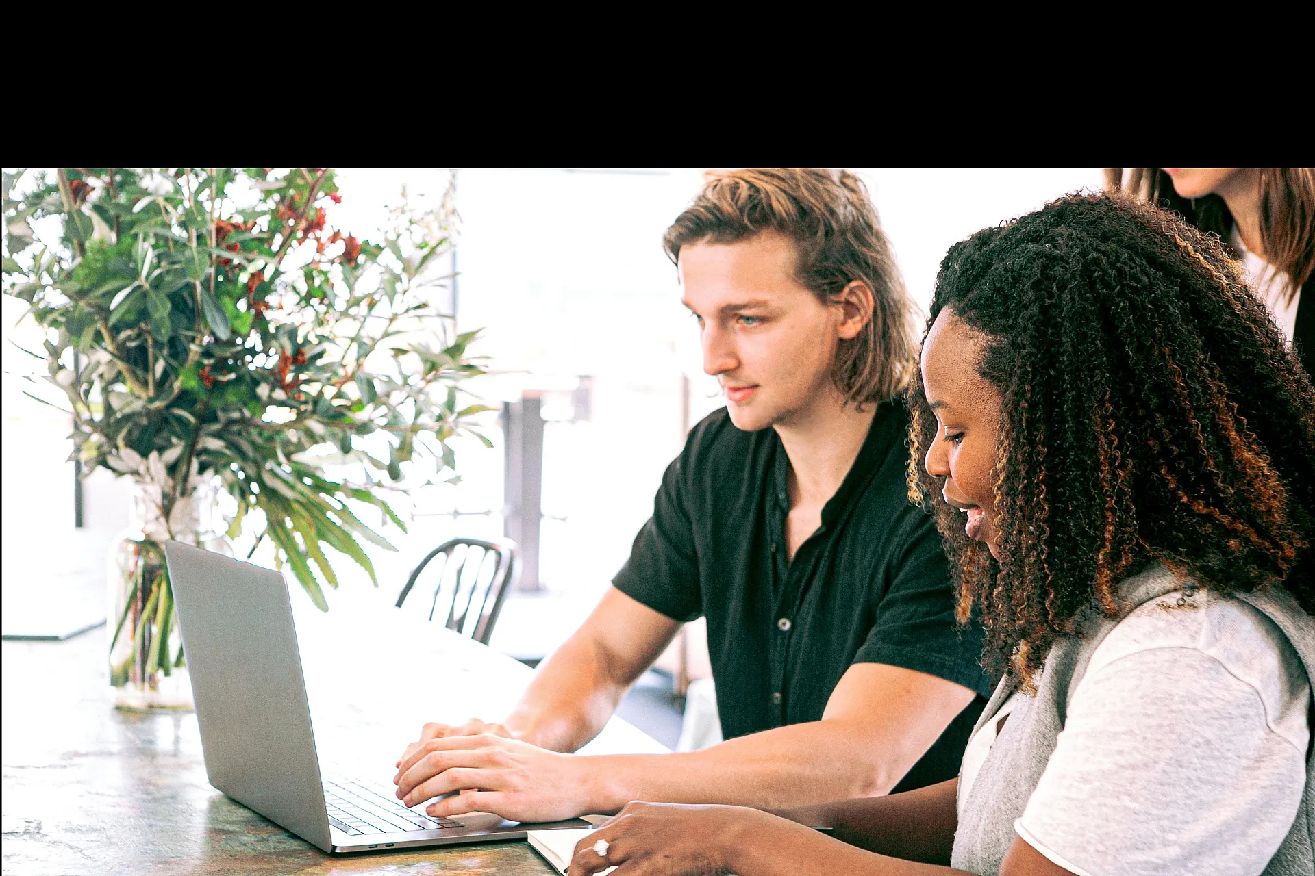Bright and modern workspace with two people collaborating on a laptop at a stylish marble table, surrounded by lush greenery.