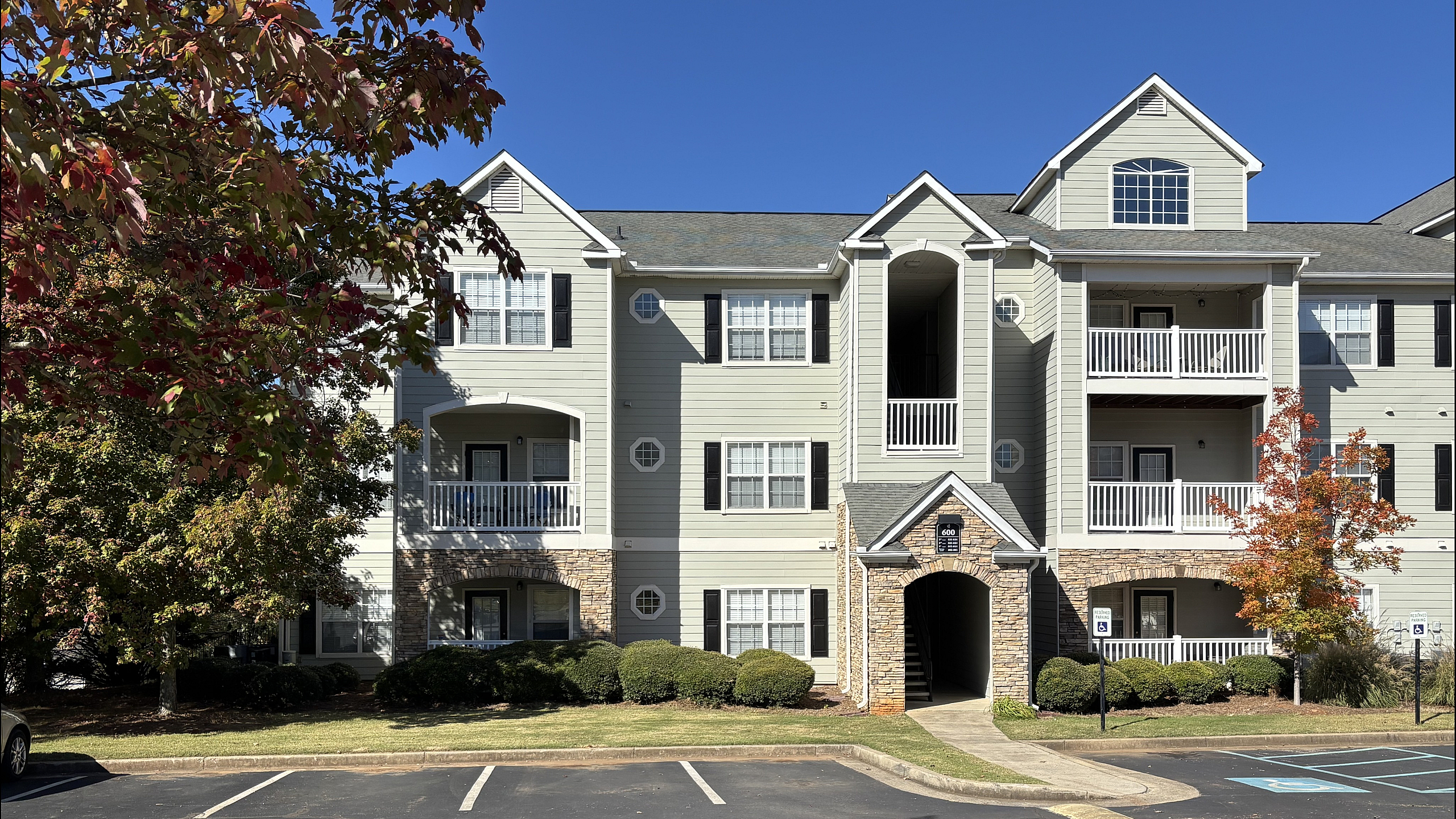 Charming apartment building exterior with classic architecture, beautiful balconies, and a lush surrounding landscape on a sunny day.