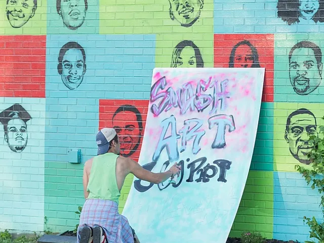 Vibrant mural featuring diverse faces painted on a colorful brick wall, with an artist creatively working on a graffiti poster titled 'Smash Art'.