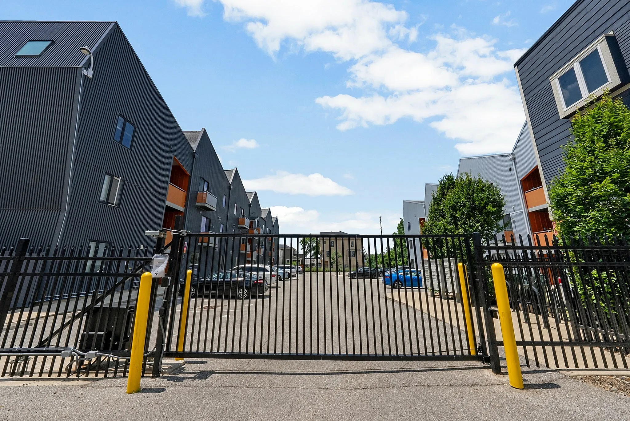 Modern gated apartment complex with sleek architectural design and ample parking space under a bright blue sky.