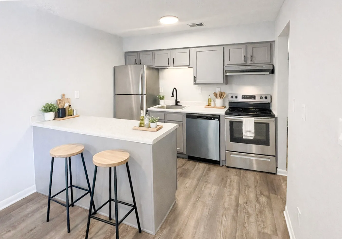 Modern kitchen with sleek appliances, stylish gray cabinetry, and a cozy breakfast bar with two wooden stools.