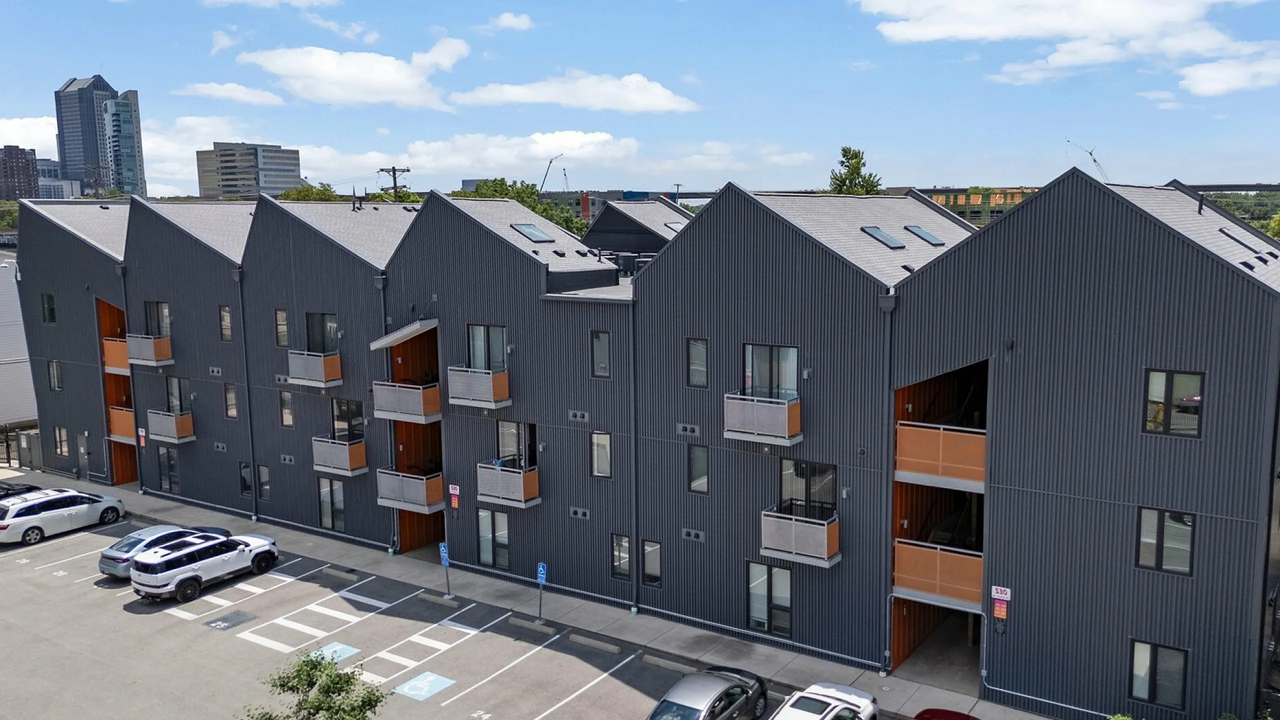 Modern urban apartment complex with unique angular design, featuring multiple balconies, convenient parking, and a vibrant city backdrop.