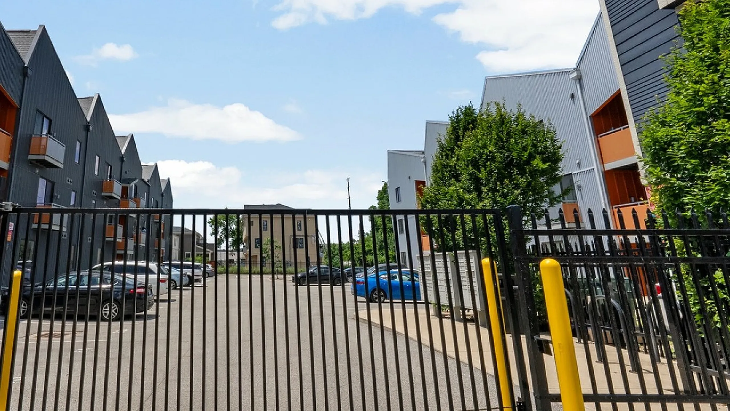 Modern gated apartment complex featuring sleek architecture, ample parking, and lush greenery under a clear blue sky.