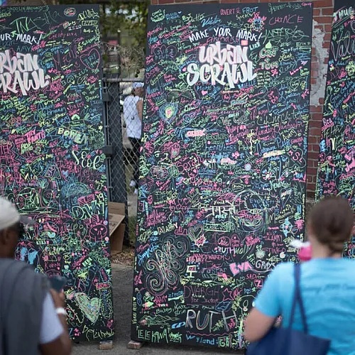 Vibrant street art panels filled with colorful graffiti and signatures, engaging people in creative expression at an outdoor festival.